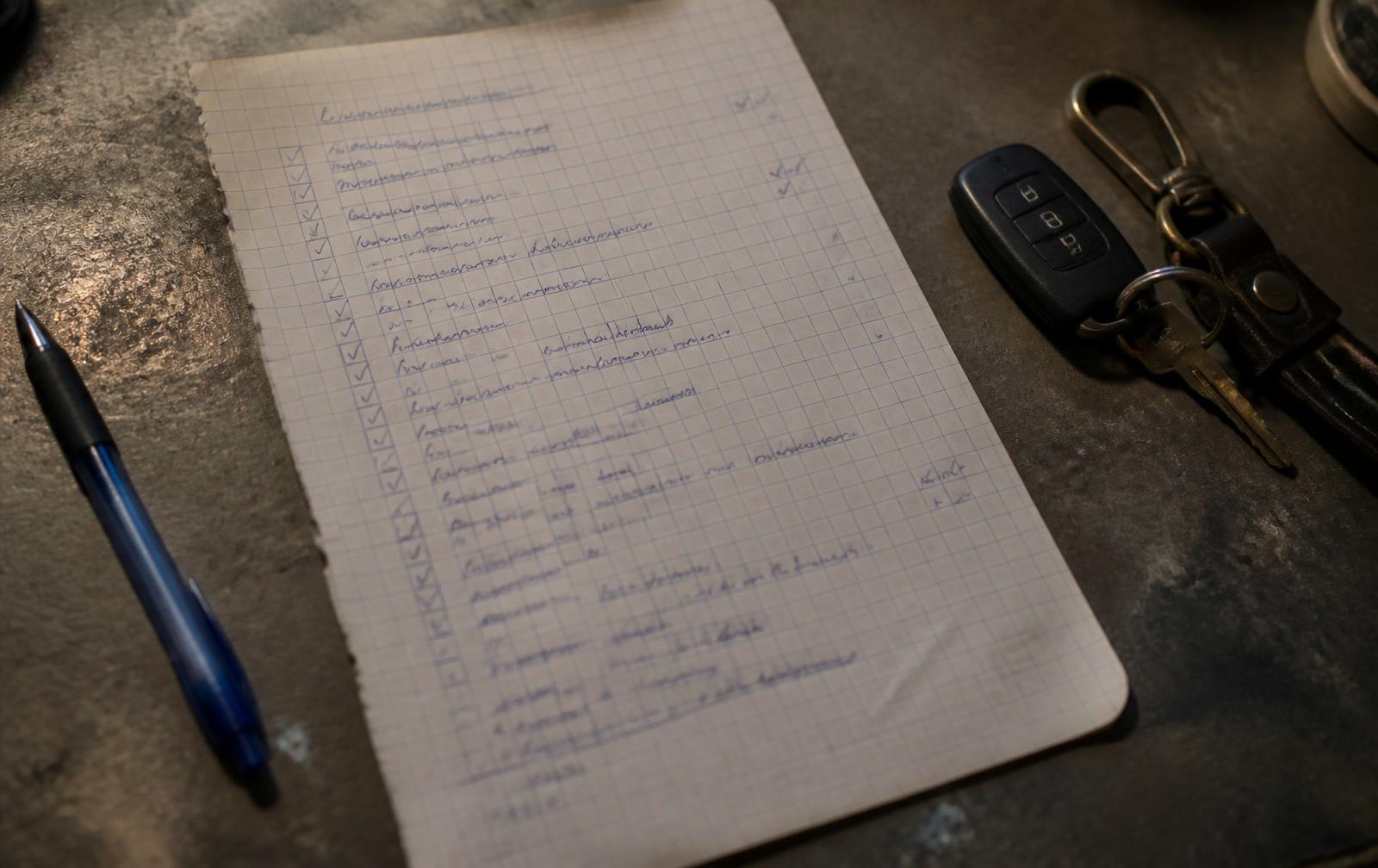 A handwritten vehicle checklist on graph paper with a pen and car keys on a workbench